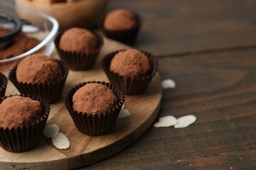 Delicious homemade candies powdered with cocoa on wooden table, closeup. Space for text