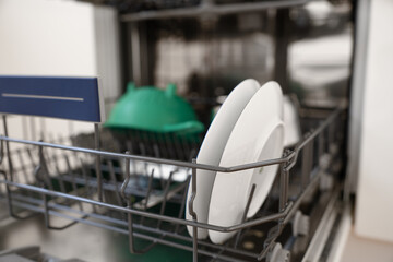 close-up view of a dishwasher interior featuring neatly arranged clean plates alongside a green colander, emphasizing organization and modern home kitchen technology