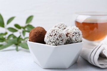 Delicious homemade candies with cocoa powder and coconut flakes in bowl on white table, closeup