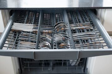 close-up view of a neatly organized dishwasher drawer filled with clean stainless steel cutlery,...