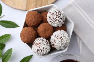 Delicious homemade candies with cocoa powder and coconut flakes in bowl on white table, flat lay