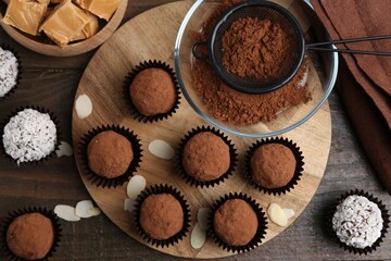 Delicious homemade candies with cocoa powder and coconut flakes on wooden table, flat lay