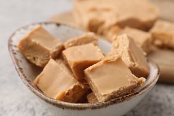 Homemade caramel candies in bowl on light grey table, closeup