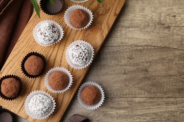 Delicious homemade candies with cocoa powder and coconut flakes on wooden table, flat lay. Space for text