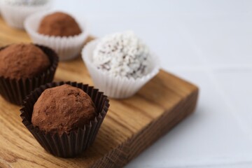 Delicious homemade candies with cocoa powder and coconut flakes on white table, closeup