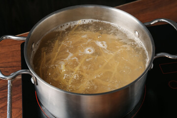 Fresh tagliatelle pasta boiling in pot with water on electric stove, closeup