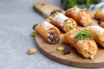 Delicious cannoli with cheese, nuts, powdered sugar, chocolate and mint on grey table, closeup. Space for text