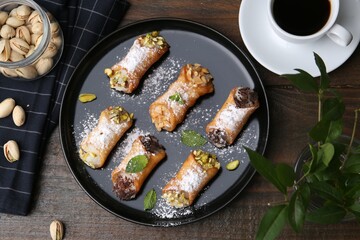 Delicious cannoli with cheese, nuts, powdered sugar, chocolate, mint and coffee on wooden table, flat lay