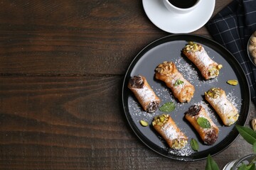 Delicious cannoli with cheese, nuts, powdered sugar, chocolate, mint and coffee on wooden table, flat lay. Space for text