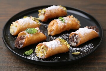Delicious cannoli with cheese, nuts, powdered sugar, chocolate and mint on wooden table, closeup