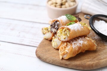 Delicious cannoli with cheese, nuts, powdered sugar, chocolate and mint on white wooden table, closeup. Space for text