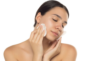 Young brunette woman cleansing her face with cotton pads, eyes closed, studio shot on white background