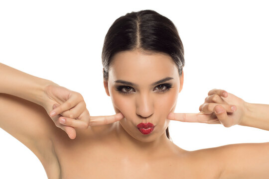Playful woman making kissy face while pulling her cheeks, studio shot on white background.