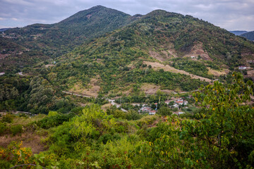 Lush green hills with scattered rural houses in Başiskele, Kocaeli, Türkiye, captured under a cloudy sky in a tranquil countryside setting.