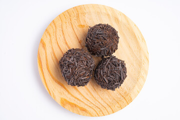 Three chocolate truffles covered with chocolate sprinkles served on a round wooden plate isolated on white background.