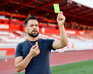 Portrait of a soccer referee blowing a whistle and showing a yellow red card on stadium soccer field