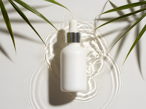 Cosmetic serum dropper bottle mockup with tropical leaves and water ripple reflection, white skincare packaging design for beauty, wellness and organic cosmetic branding.
