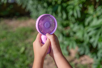 Hand holding portable mini fan outdoors in sunlight