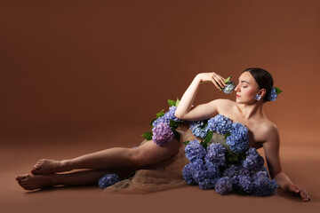 Beautiful young woman with hortensia flowers on brown background. Space for text