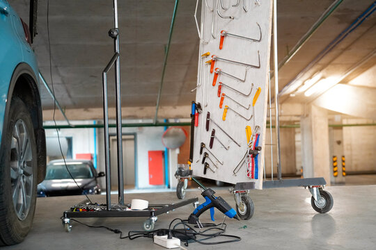 Light blue sport utility vehicle is parked inside a garage and is being worked on using paintless dent repair tools and equipment. The hatch is open to improve access