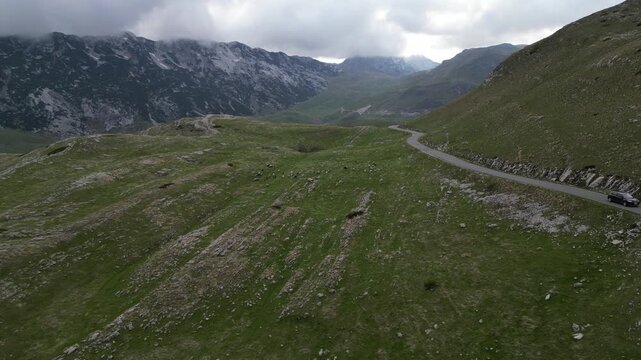 4K aerial drone footage flying forward and descending into scenic mountain valley with P14 road and grazing sheep Durmitor Montenegro