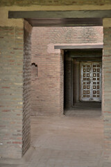 A narrow corridor featuring exposed brick walls and flooring leads to a door with a geometric wooden panel design.