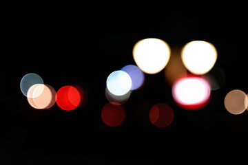 Out-of-focus city lights at night create a bokeh effect. Red, white, and blue circles of light are prominent against a dark background.