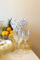 Delicate heart-shaped decor made of twigs sits gracefully among crystal glasses, reflecting a warm ambiance. Surrounding fruits and a cake hint at a joyful celebration with loved ones.
