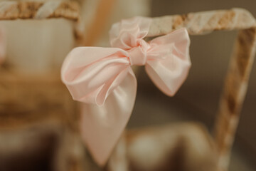 A delicate pink satin bow adorns a charming wooden chair, bringing a touch of elegance to the cozy interior. Warm sunlight filters through, enhancing the aesthetic warmth of the space.