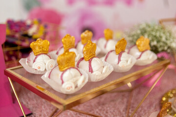 Colorful confections adorned with golden crowns rest on a stylish tray at a festive gathering, embodying creativity and sweetness. Each piece is intricately designed for a delightful experience.