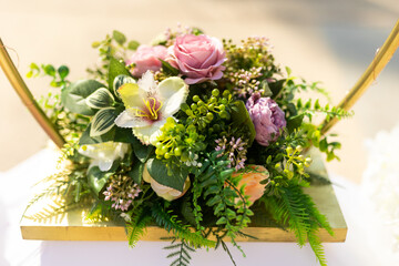 A beautiful floral arrangement bursts with color in a golden basket, featuring roses, orchids, and lush greenery. The scene captures the joy of a festive celebration in sunlight.