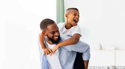 Happy Loving Family. Cheerful African American man and woman having fun with children in living room, giving smiling boy and girl piggyback ride. Four positive black people spending time together