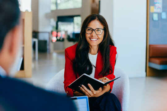 Smiling businesswoman in red blazer with notebook at a meeting