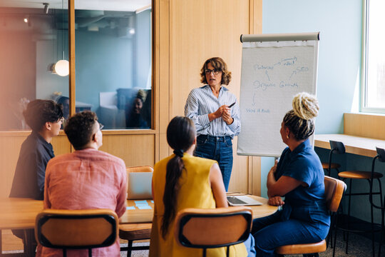 Woman presenting business strategies to a diverse group in a discussion - Powered by Adobe