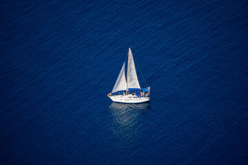 Yacht with white sails on a blue sea background. Top view.