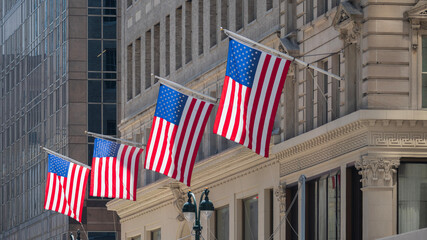 Four American flags waving on the facade of a building on a sunny day.