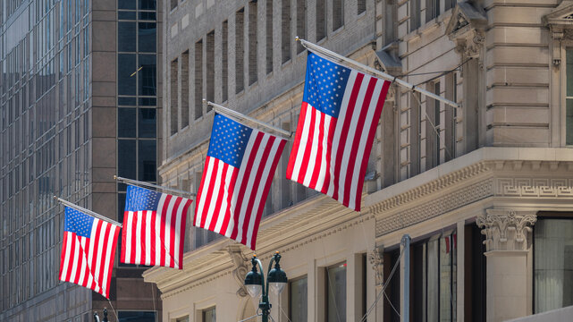 Four American flags waving on the facade of a building on a sunny day.