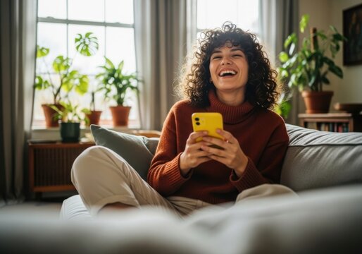 Happy woman laughing while holding a yellow smartphone on a couch