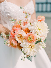 Beautiful bridal bouquet of peach and white flowers held by a bride on her wedding day outdoors