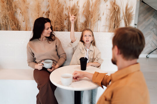Curious daughter raises hand confidently while talking, parents listening attentively, highlighting empowered communication in mindful, tech-light family moment.