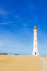 California Lighthouse in desert landscape of Aruba against background of blue sky with white clouds.