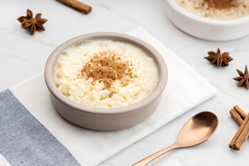 Creamy rice pudding with cinnamon in bowl on white marble table