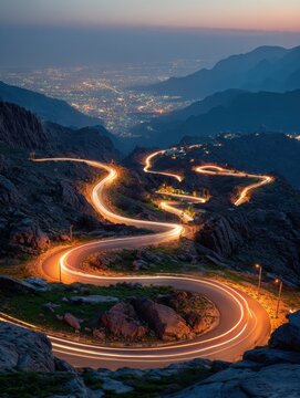 zigzag mountain road features car light trails at dusk in al hada taif saudi arabia illuminated city lights glow below rocky landscape as vehicles create streaks of light on winding highway