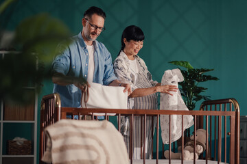Loving couple arranging baby clothes in crib, preparing for parenthood