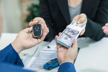 buyer is receiving the car keys from the car dealer after completing the sales contract and paying the dealer. dealer hands the car keys to the customer in the office after completing sales contract.