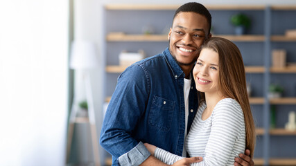 Fototapeta premium Portrait Of Young Loving Multiracial Couple Embracing At Home, Smiling Happy Millennial Black Man And White Woman Hugging In Living Room, Enjoying Spending Time Together, Copy Space