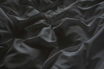 Dark fabric with soft folds and shadows creating abstract texture and moody background

