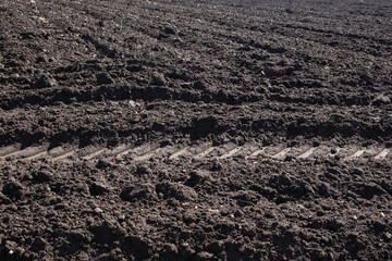 Cultivated plowed soil with rows and tractor footprint. Agricultural background texture