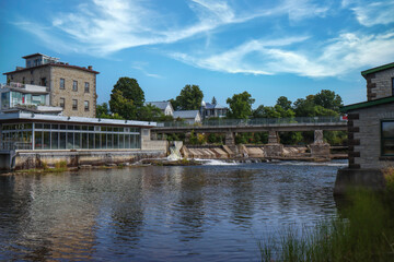 Small hydroelectric power station along river rapids and waterfall, footbridge, daytime, sunny, nobody