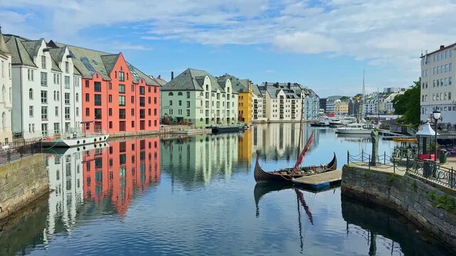 &Aring;lesund, Norway: Art Nouveau colorful buildings reflected in Brosundet canal with moored viking ship